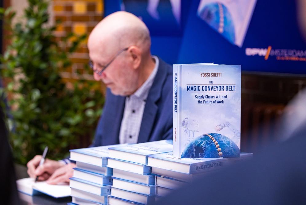 Sheffi signing books next to stack of "The Magic Conveyor Belt"